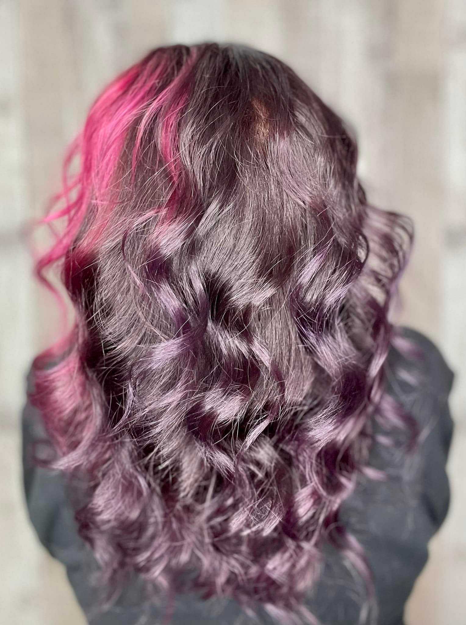 Person with long, wavy black hair featuring purple and pink highlights, facing away from the camera.