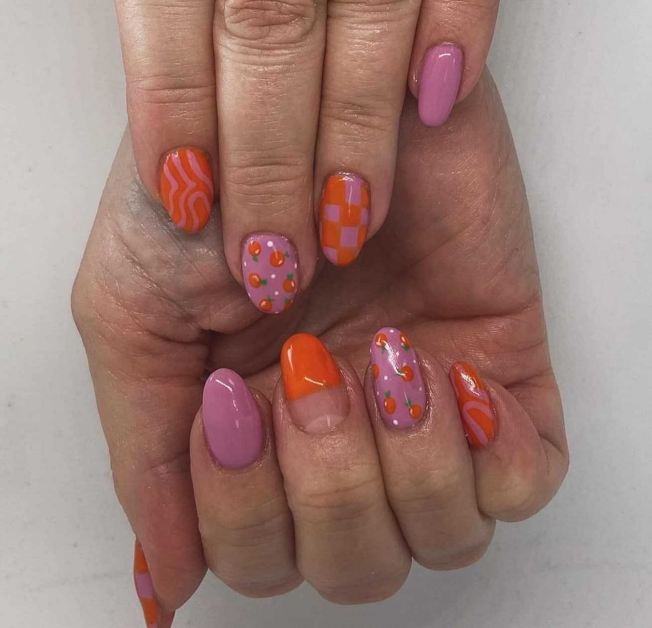 Colorful nail art with pink, orange, checkered, and abstract designs on a woman's hands.