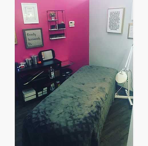 Cozy massage room with a pink accent wall, treatment table, and various beauty products on shelves.